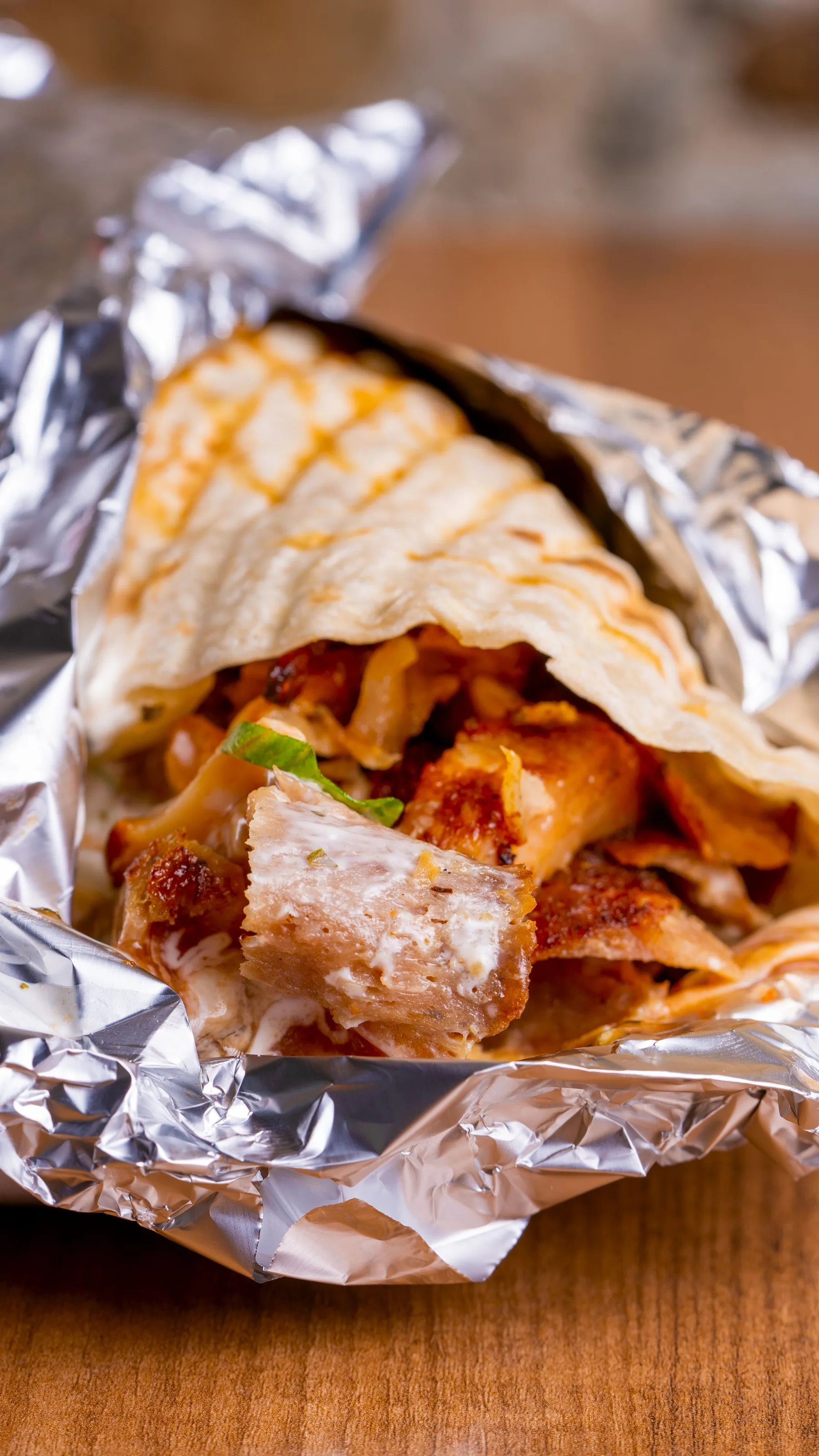 A chicken shawarma laffa opened in foil, showing crisp chicken and garlic sauce